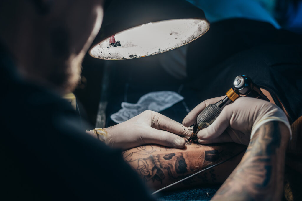 Tattoo artist hands in a white gloves holding a machine while creating a tattoo on a woman hand